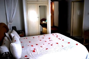 Una habitación de hotel con una cama, cortinas blancas, un armario y un espejo.