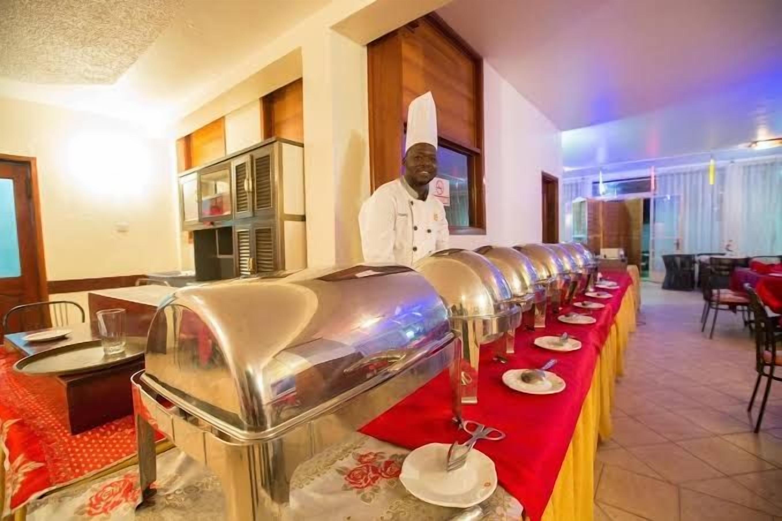 Disposição de buffet com diversas estações de serviço, um chef e área de refeições com mesas e cadeiras.