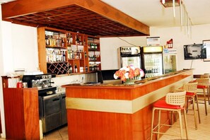 Eine Bar mit Holztresen, Barhocker, einem Kühlschrank und einem an der Wand befestigten Fernseher.
