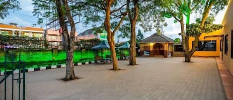 An outdoor area with trees, a paved walkway, and a building with a green awning.