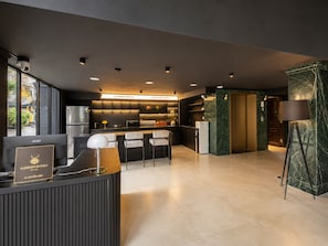 Una moderna hall d'albergo con reception, area salotto e una cucina sullo sfondo.