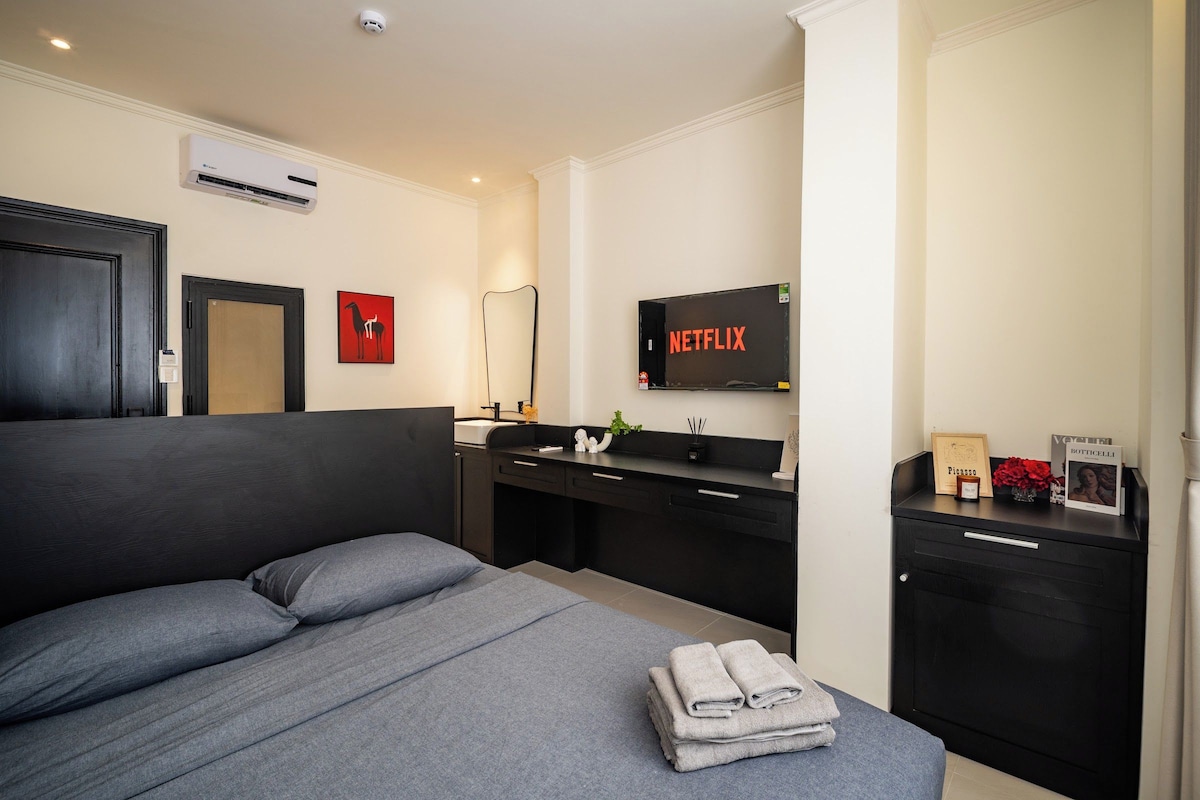 Una camera da letto moderna con un letto grande, un comodino, una TV e un bagno con lavandino e specchio.