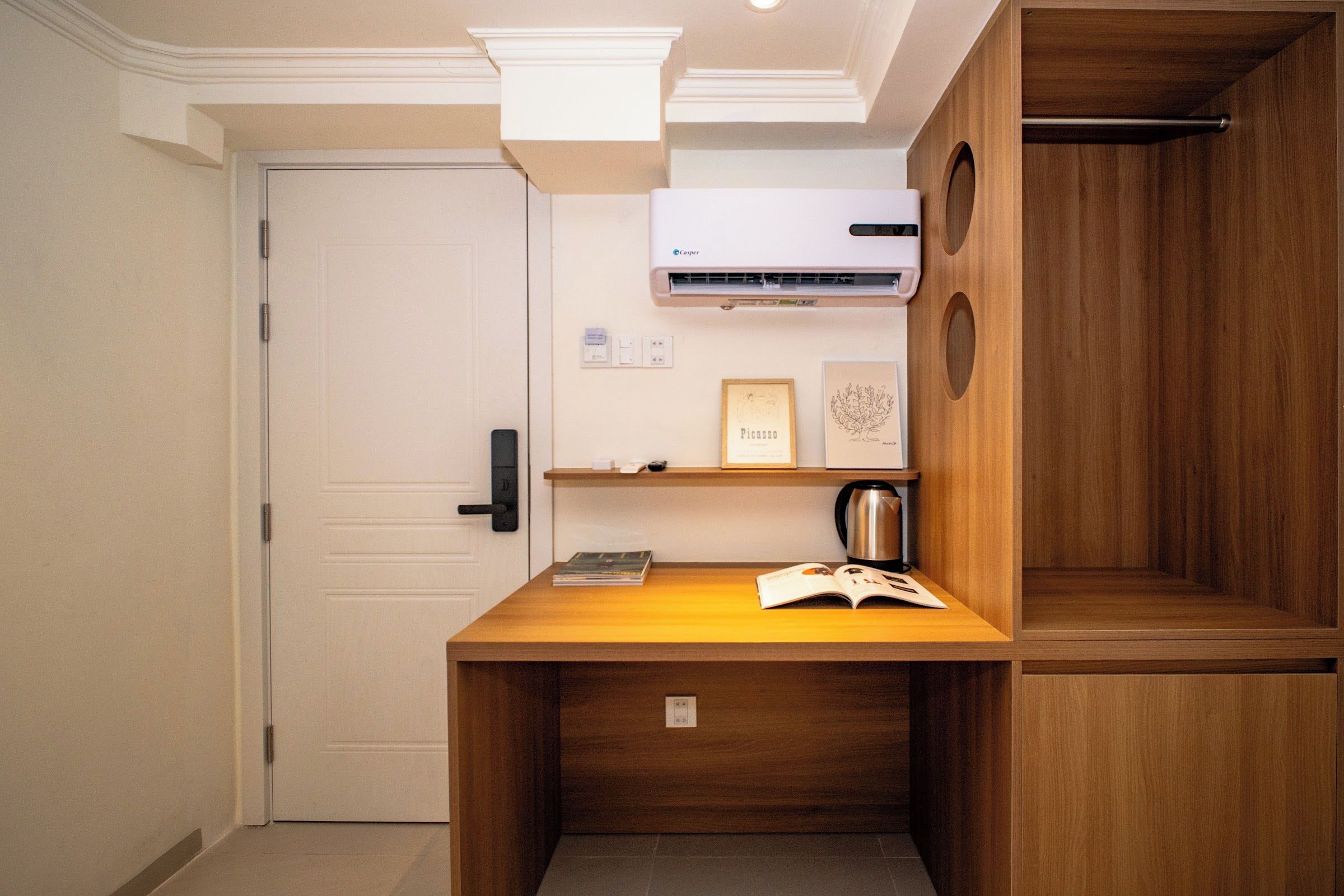 Une pièce de taille modeste, comprenant un bureau en bois, une bibliothèque, une œuvre d’art encadrée et une machine à café.