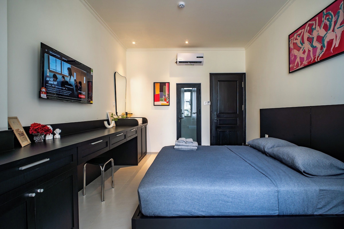 Una camera da letto moderna con un letto, una scrivania, una sedia, una TV e opere d'arte alle pareti.