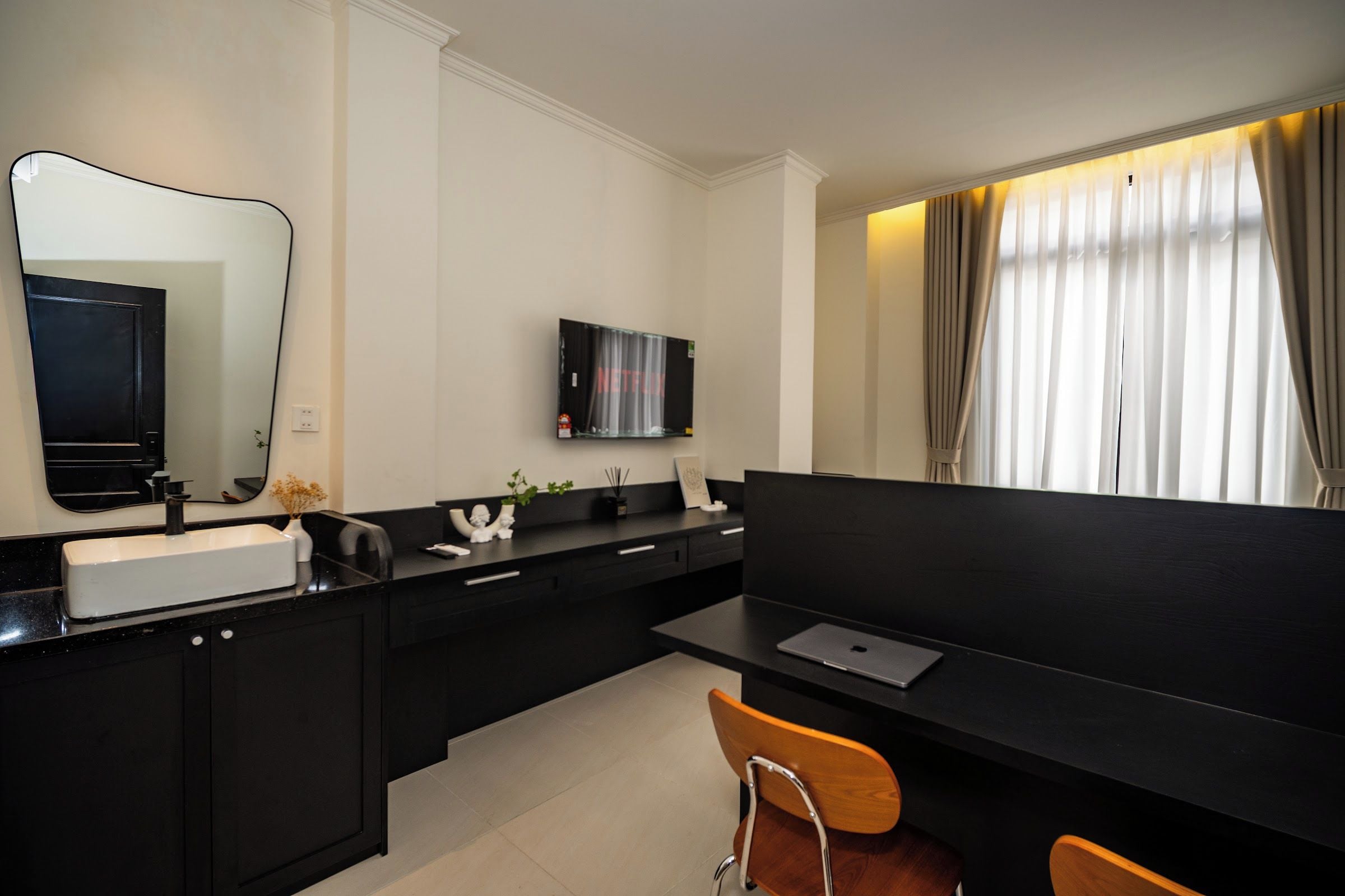 Une cuisine moderne avec un plan de travail noir, un évier, un miroir, un téléviseur à écran plat fixé au mur et un coin repas avec une table et deux chaises.