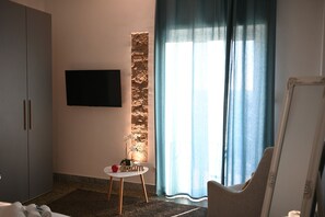 A hotel room with a flat-screen TV mounted on the wall, a small round table with a vase and a red object, a large window with curtains, and a wardrobe. - New Listing (Lido di Ostia)