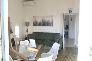 A living room with a green sofa, a glass coffee table, and a painting on the wall. - New Listing (Lido di Ostia)