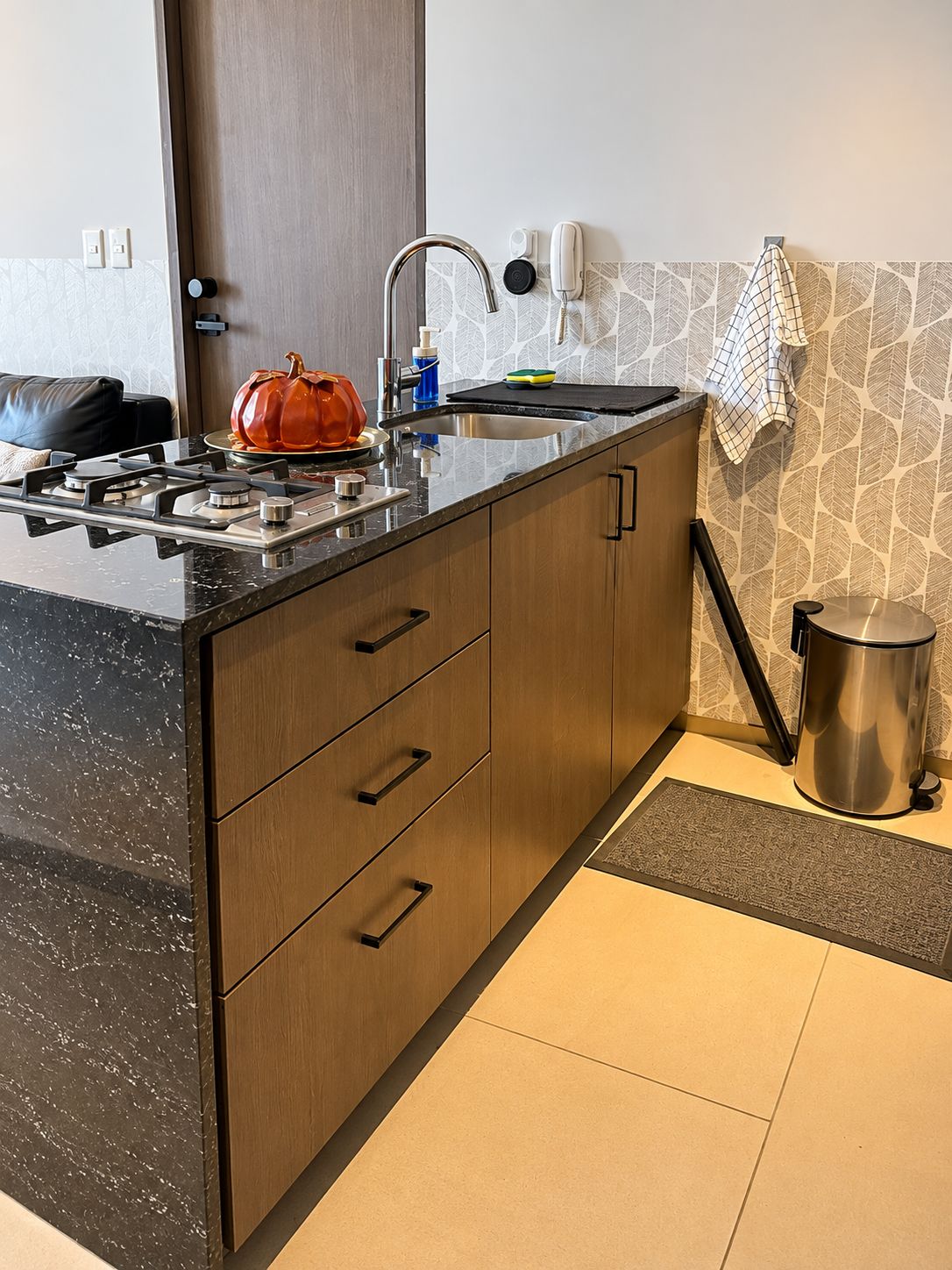 A modern kitchen with a black marble countertop, wooden cabinets, a stainless steel sink, and a coffee machine.