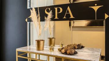 A spa reception area with a gold-framed console table, pampas grass in gold pots, and a 'SPA' sign above.