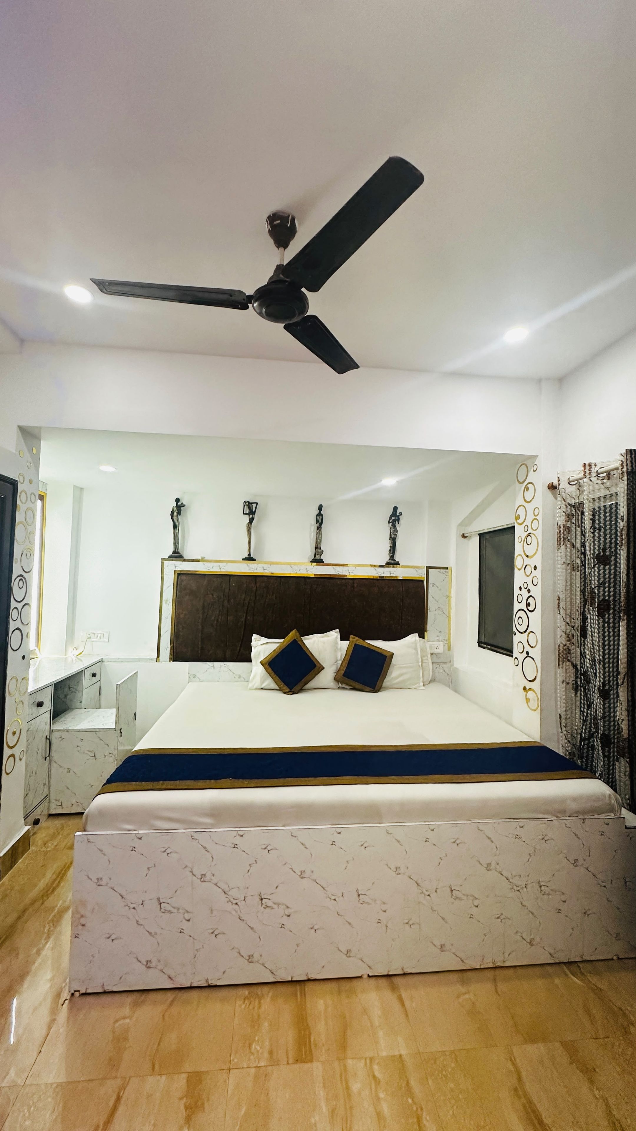 A bedroom with a bed, a ceiling fan, a headboard, and wall-mounted statues.