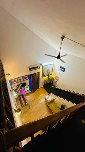 A staircase leading to a living area with a ceiling fan, a wooden door, and a small table with a lamp. - In the heart of Goa, where the rhythm of the waves meets the melody of the villa (Calangute)
