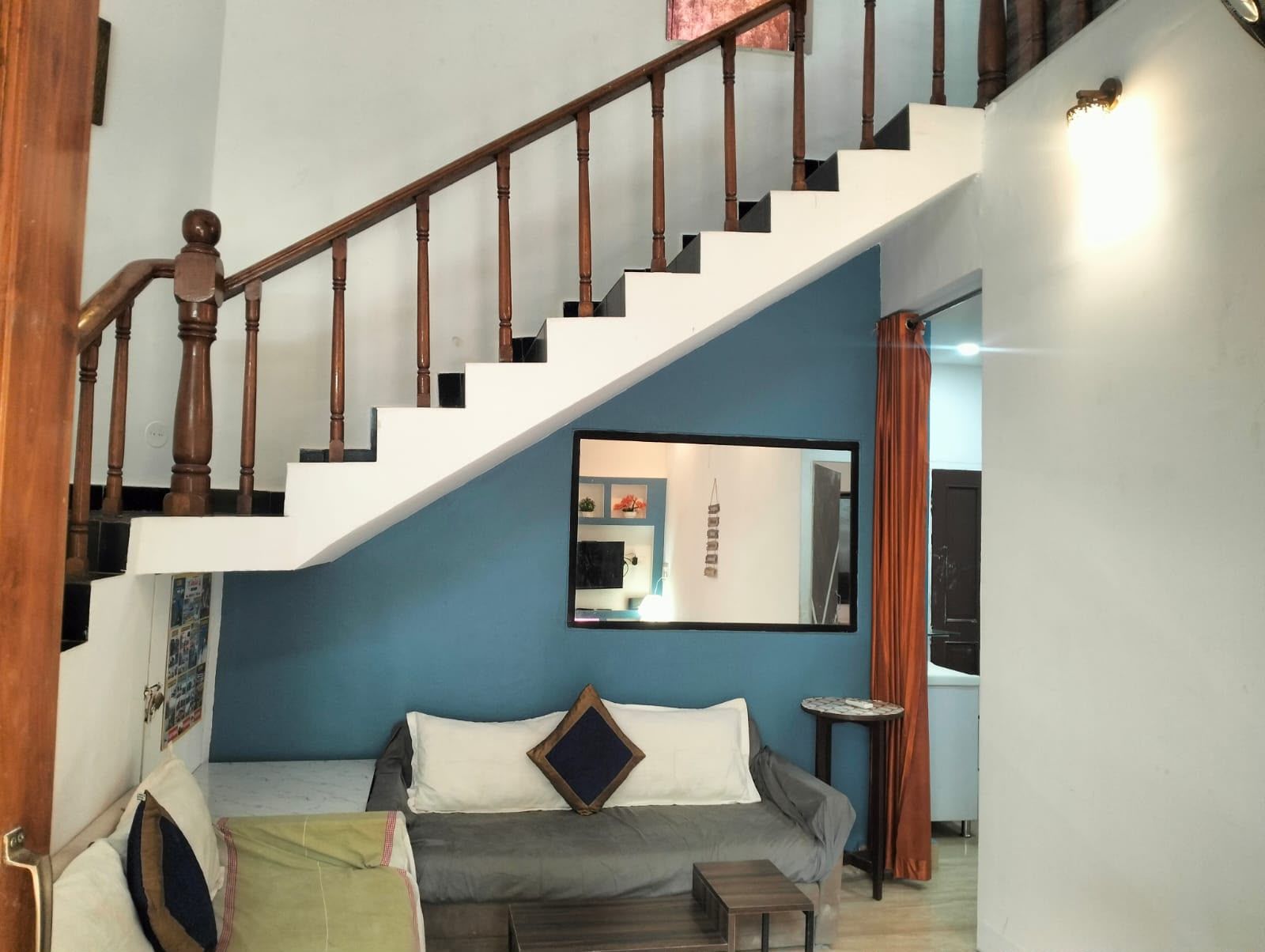 A staircase with wooden balusters leading to a landing, a sofa with cushions, a small round table, and a wall-mounted mirror reflecting part of the room.