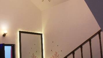 A room with a chandelier, a staircase, a sofa with patterned cushions, and a wall-mounted picture frame.