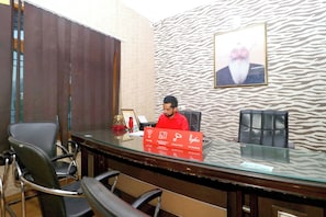 Un salón de conferencias con una mesa de vidrio, sillas de cuero negro, un cuadro en la pared y un letrero rojo con iconos.