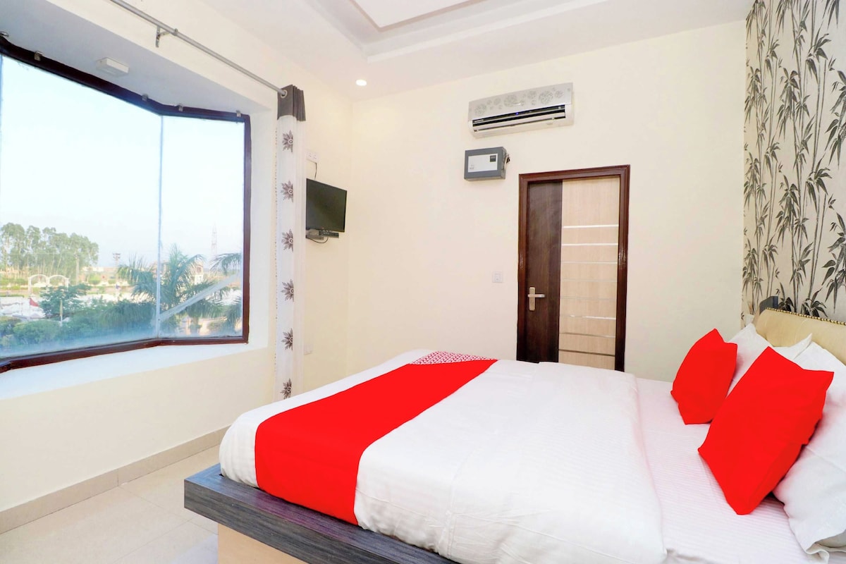 Habitación de hotel con cama, televisión, aire acondicionado, ventana con vistas y una puerta.