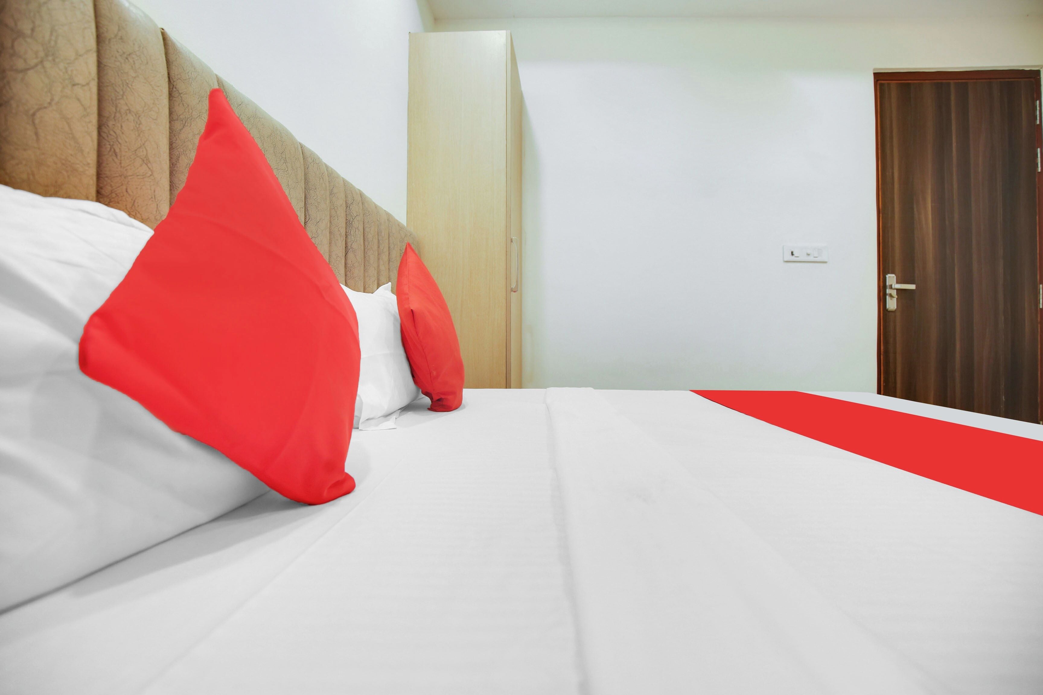 Une chambre d’hôtel avec un lit, une tête de lit en bois, un mur blanc et une porte.