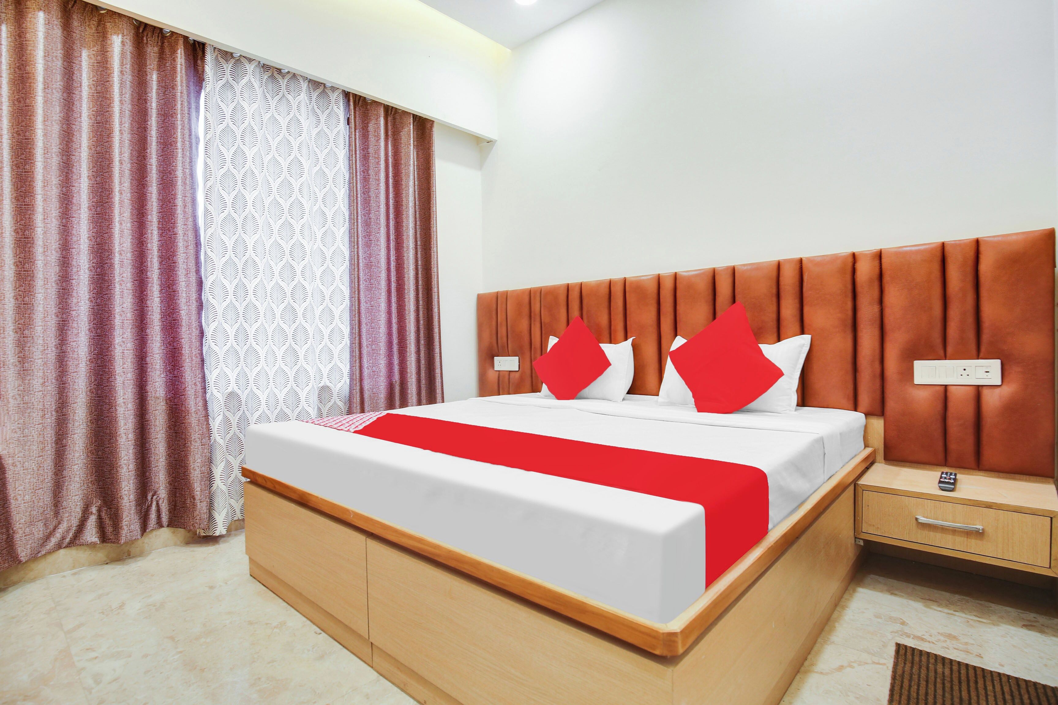 A hotel room with a bed, a nightstand, a remote control, and a power outlet.