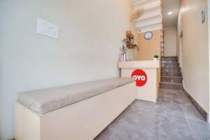 A hotel reception area with a bench, a clock, and a staircase leading to the upper floor.