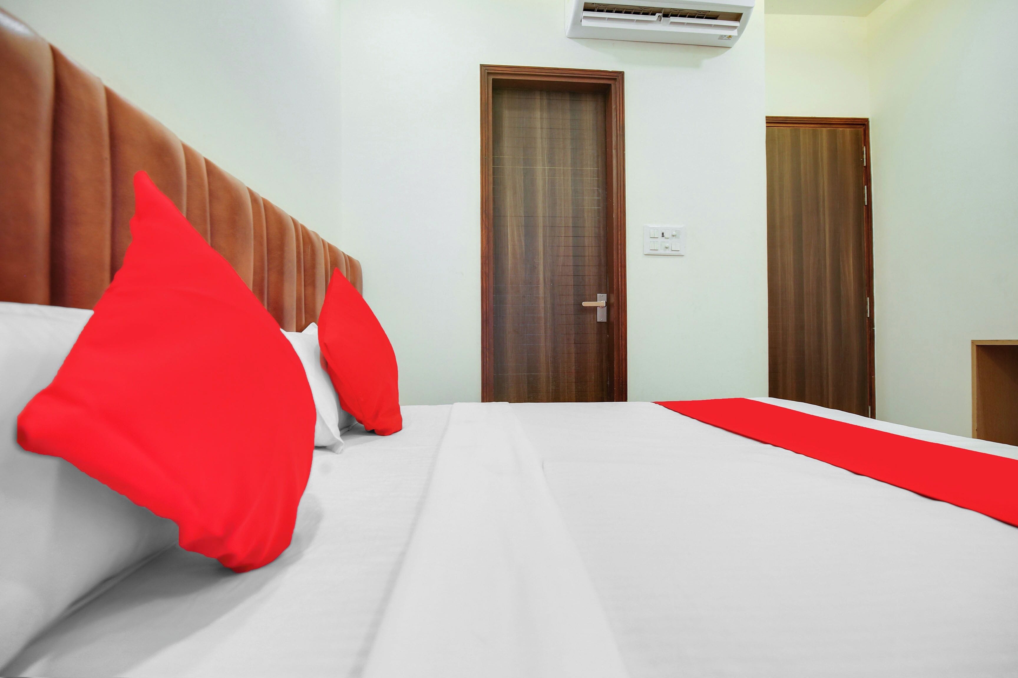 A hotel room with a bed, a wooden headboard, a door, and an air conditioning unit.