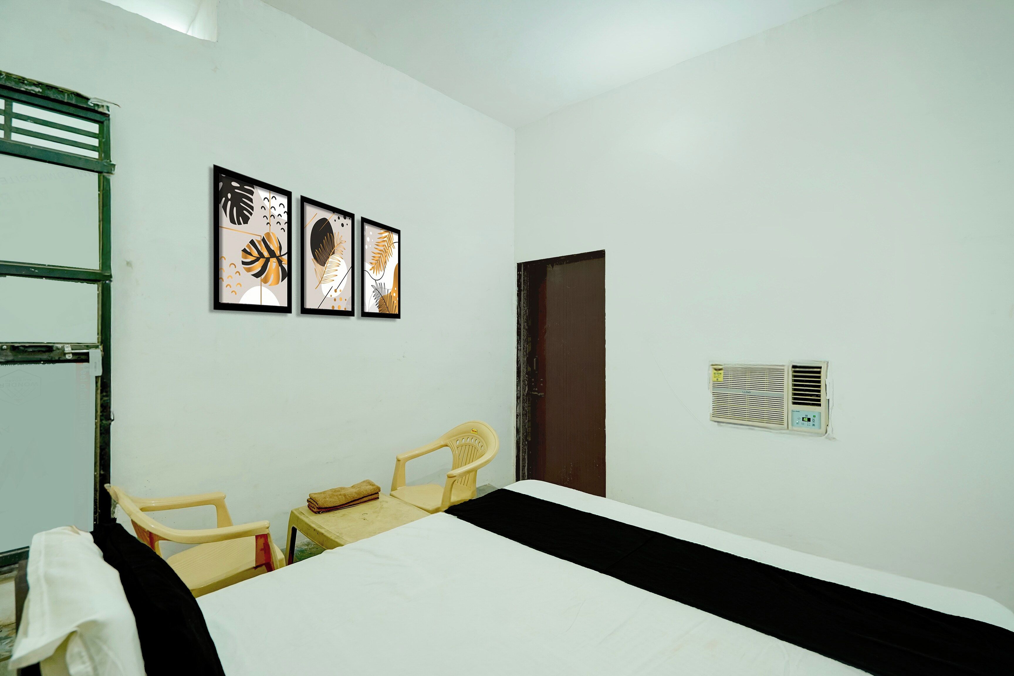 A room with a bed, two chairs, a radiator, and three framed pictures on the wall.