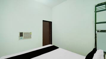 A room with a bed, a door, a wall-mounted air conditioning unit, and a towel rack.