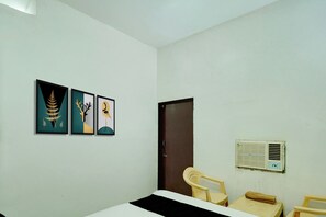 A room with a bed, a chair, a small table, and three framed artworks on the wall. - Hotel O CHOUDHARY GUEST HOUSE (Kishangarh Bas)