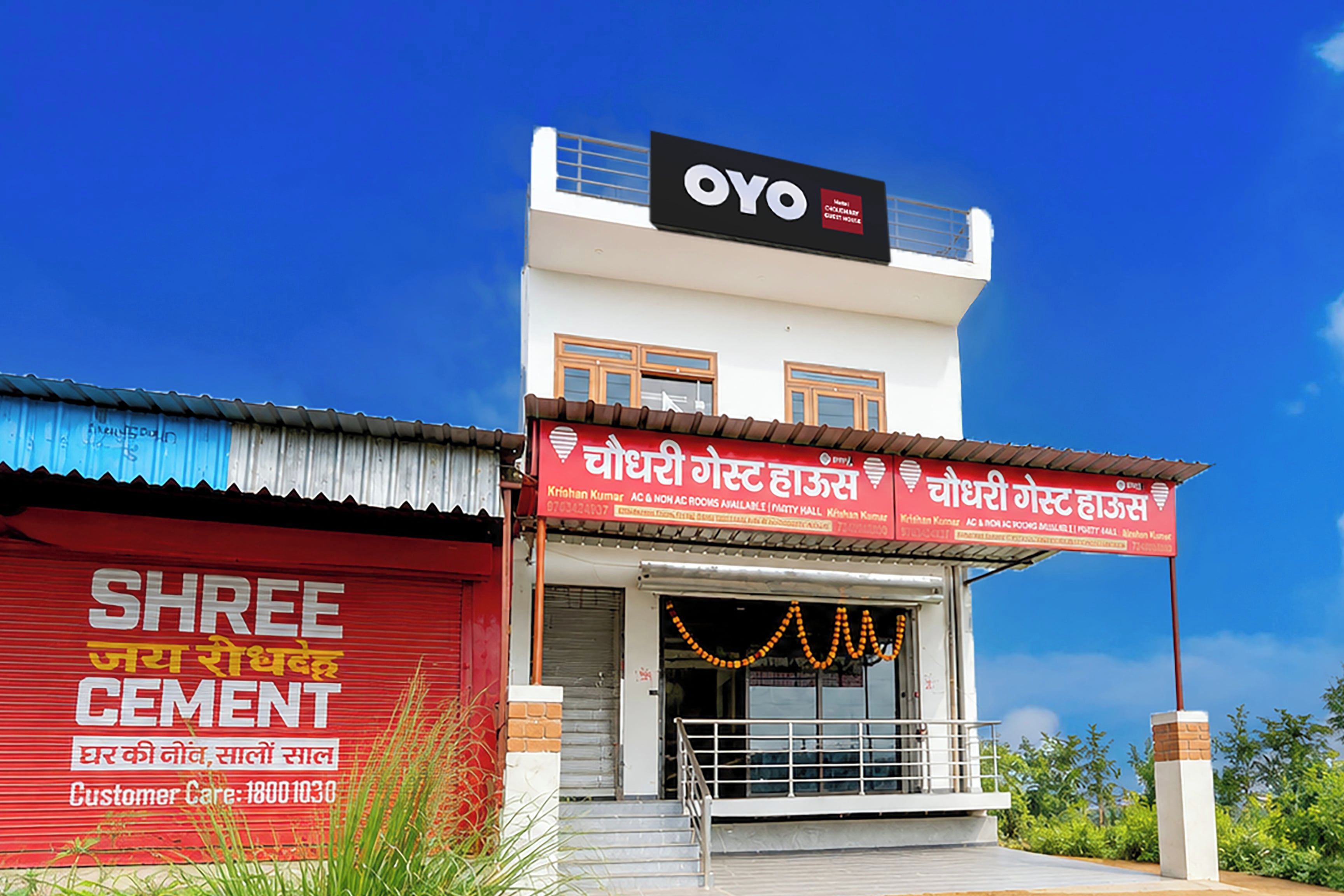 Un edificio con un cartel que dice 'OYO' y otro cartel para 'Shree Cement' con un número de atención al cliente.