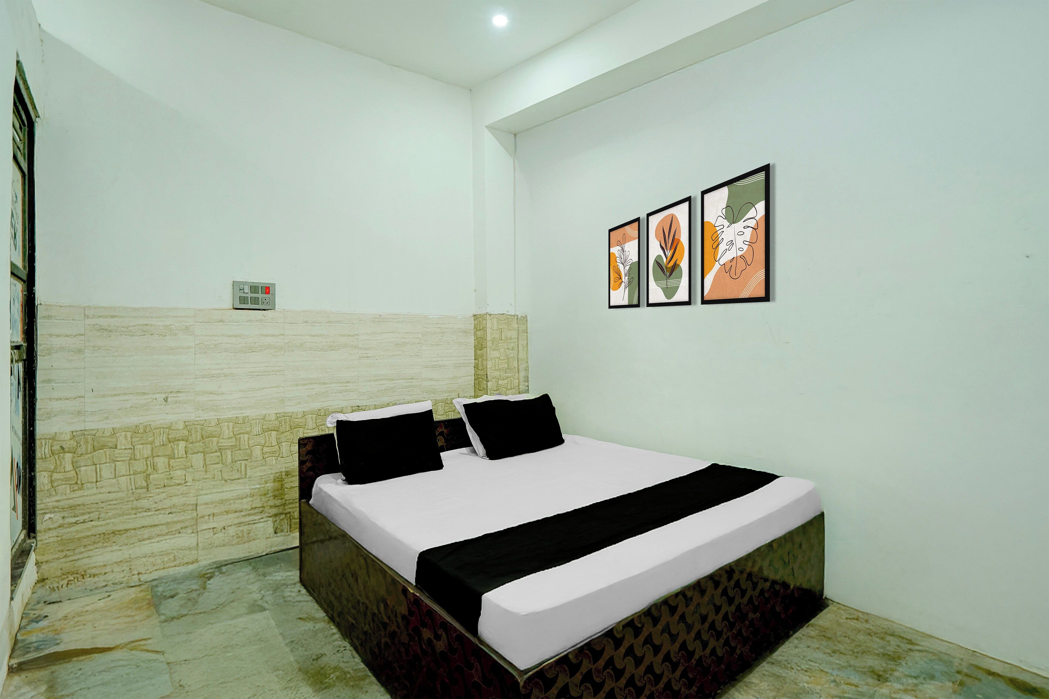 A bedroom with a bed, a wall-mounted power outlet, and two framed artworks.