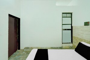 A small, simple room with a bed, a door, and a window. - Hotel O CHOUDHARY GUEST HOUSE (Kishangarh Bas)