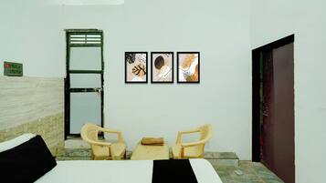 A room with a bed, two chairs, a wall-mounted power outlet, and three framed artworks.