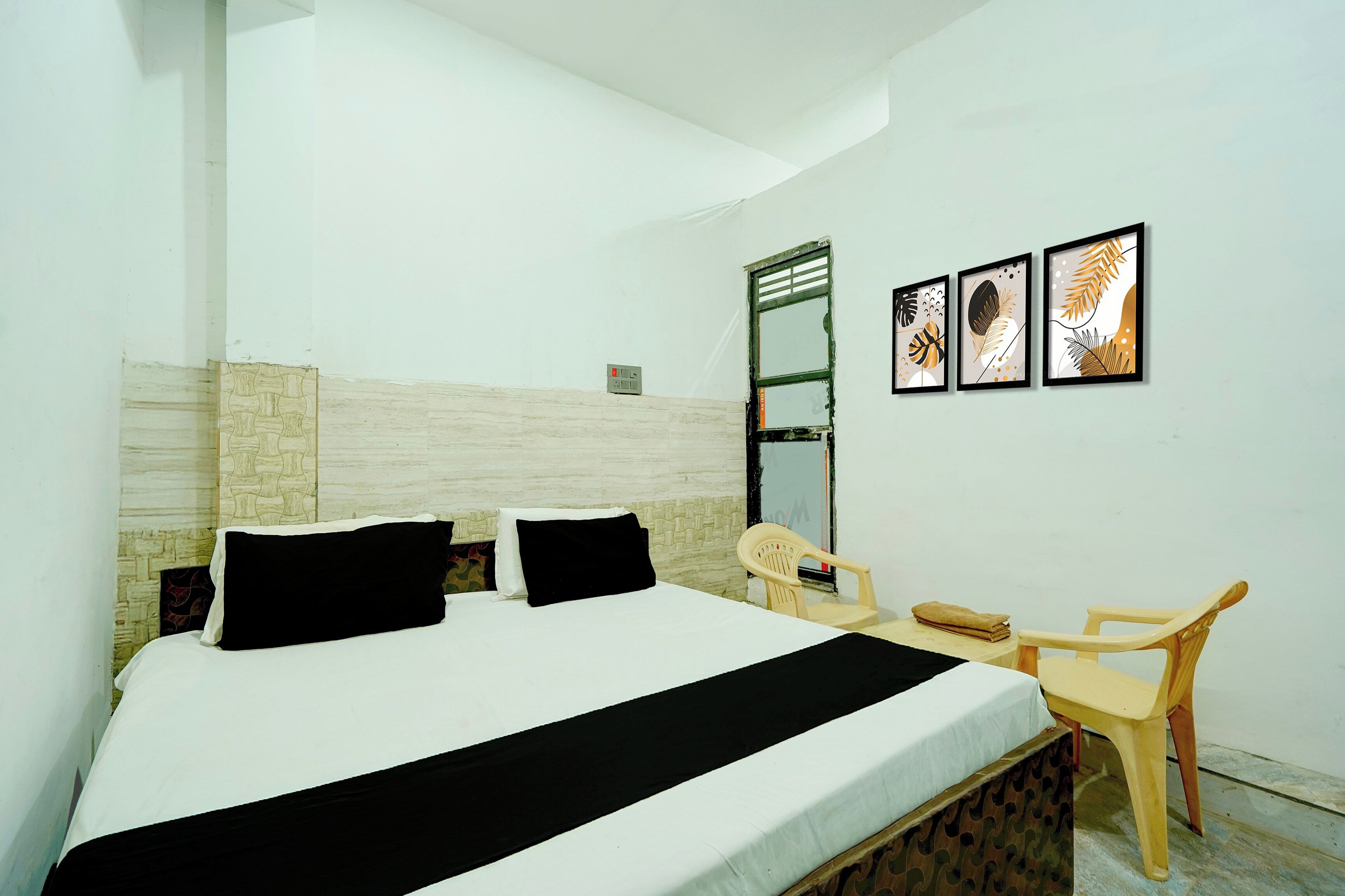 A hotel room with a bed, a desk, a chair, and three framed artworks on the wall.