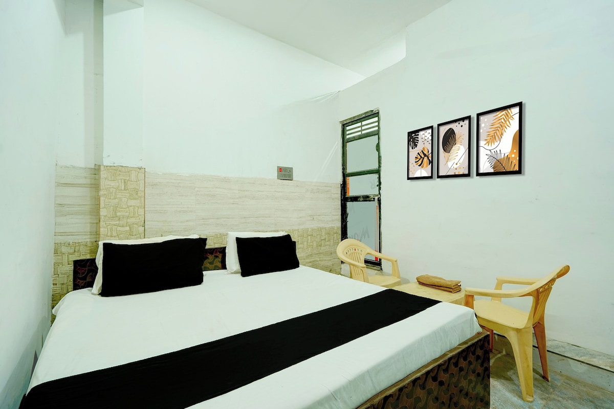 A hotel room with a bed, a desk, a chair, and three framed artworks on the wall.