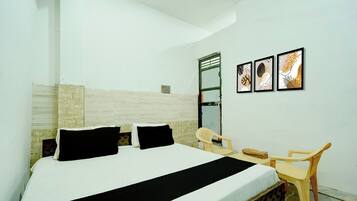 A hotel room with a bed, a desk, a chair, and three framed artworks on the wall.