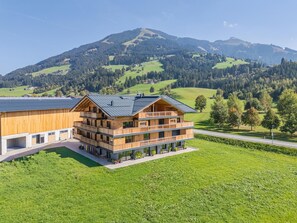A multi-story wooden building with balconies, set against a backdrop of green hills and mountains. - Apartment with sauna & balcony in Westendorf (Westendorf)