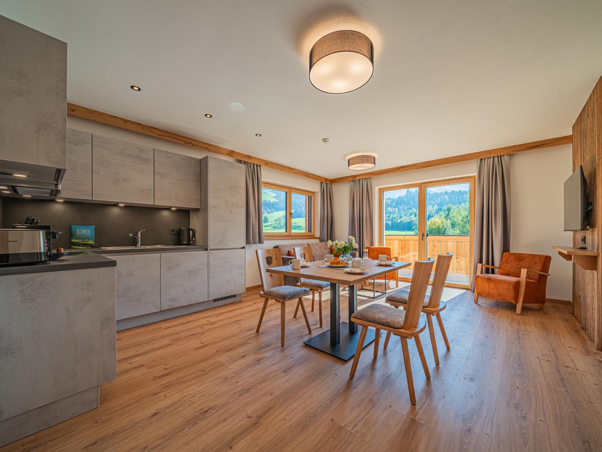 A modern kitchen with built-in appliances, a dining area with a wooden table and chairs, and large windows offering a view of the outdoors.