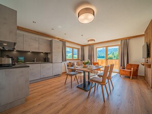 A modern kitchen with built-in appliances, a dining area with a wooden table and chairs, and large windows offering a view of the outdoors.