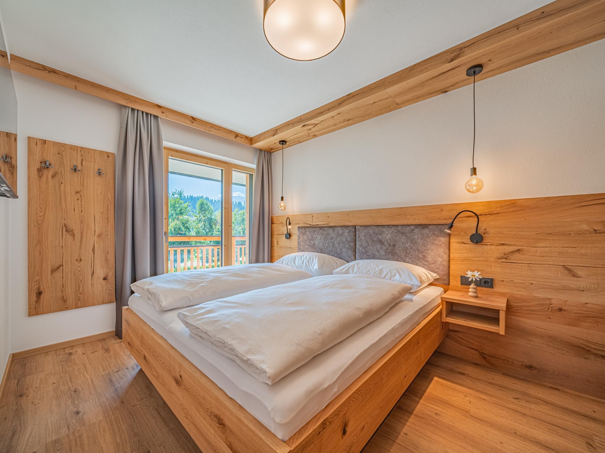 Ein Schlafzimmer mit einem hölzernen Bett, einem Nachttisch, einer Wandlampe und einem Fenster mit Vorhängen.