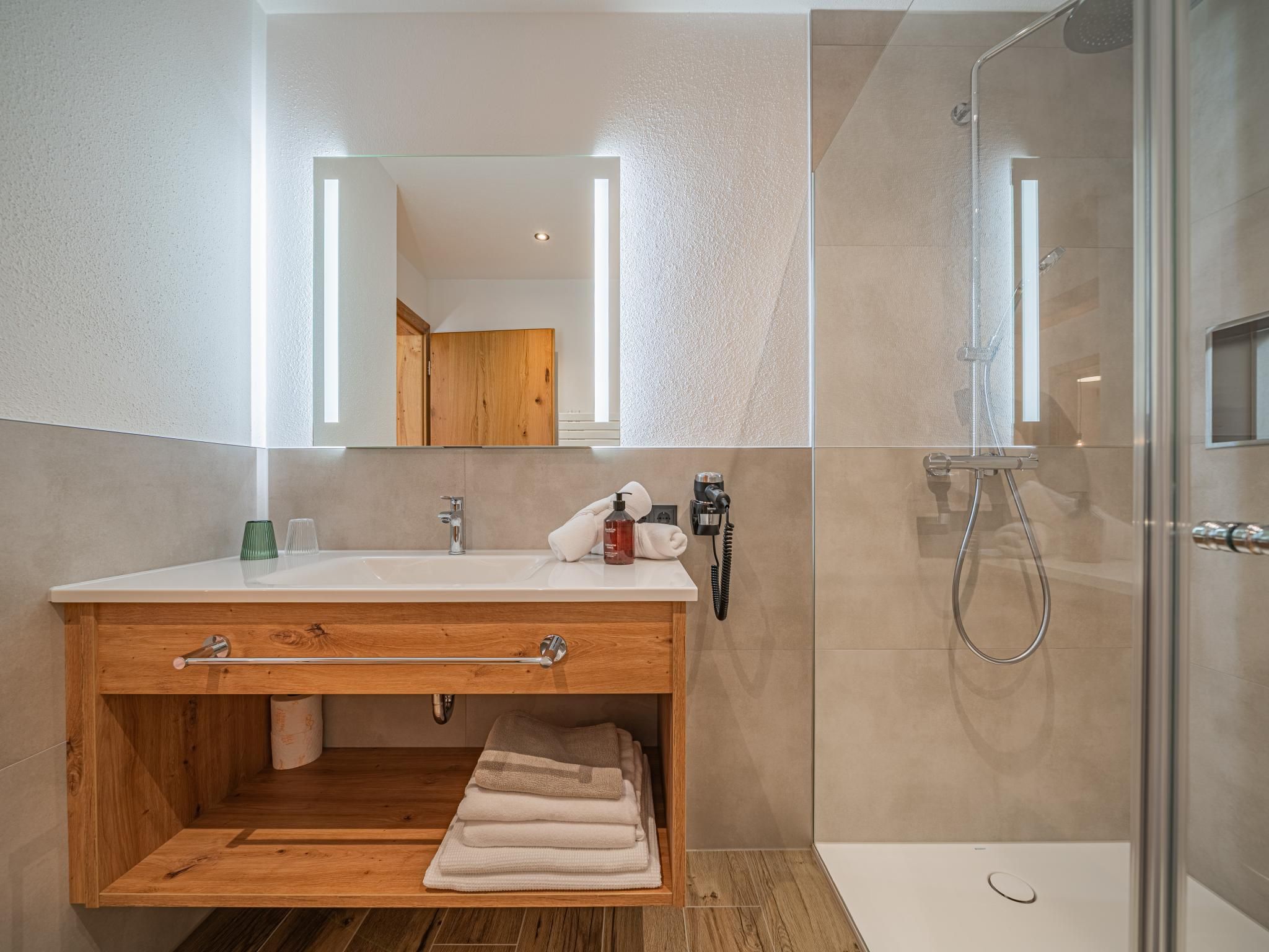 A modern bathroom with a wooden vanity, a glass shower enclosure, and a large mirror.