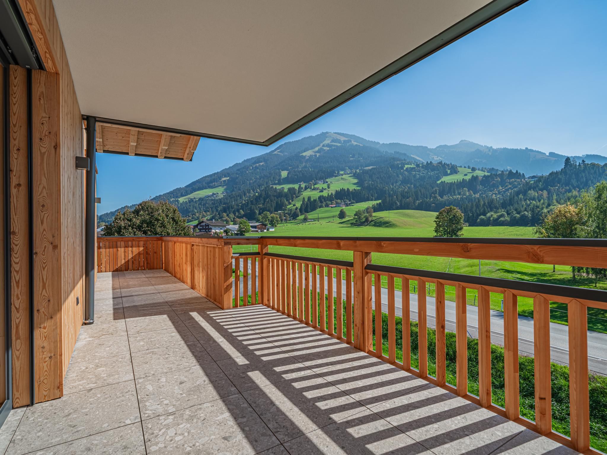 A wooden balcony with a view of green fields and mountains.