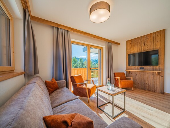 A modern living room with a sofa, chairs, a coffee table, and a TV mounted on a wooden wall. - Apartment with sauna & balcony in Westendorf (Westendorf)