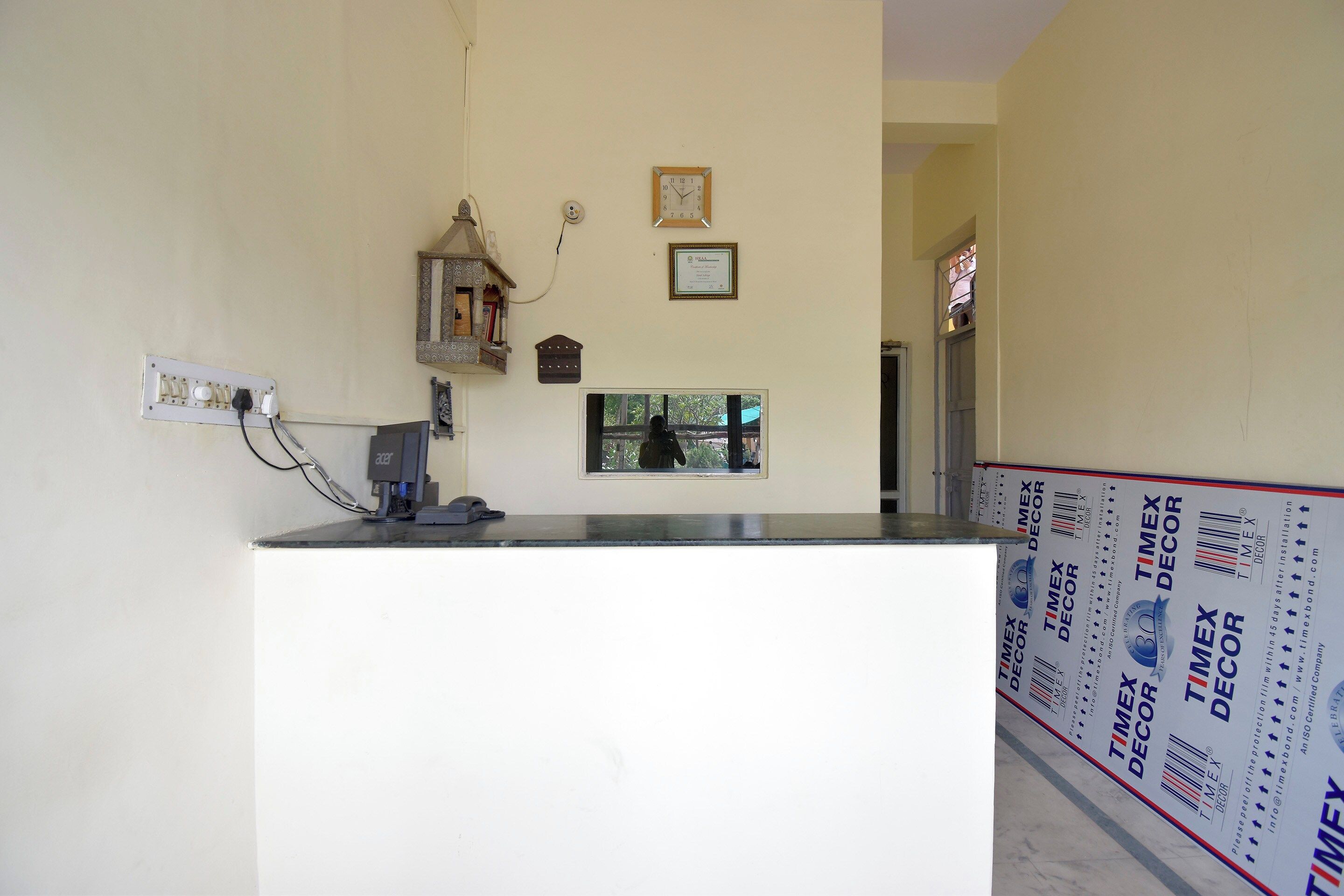 A reception desk with a computer, a wall-mounted clock, and a small window.