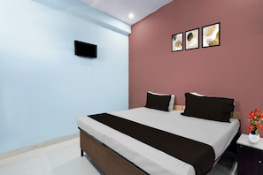 Un dormitorio con cama, mesita de noche, televisor instalado en la pared y tres cuadros enmarcados.