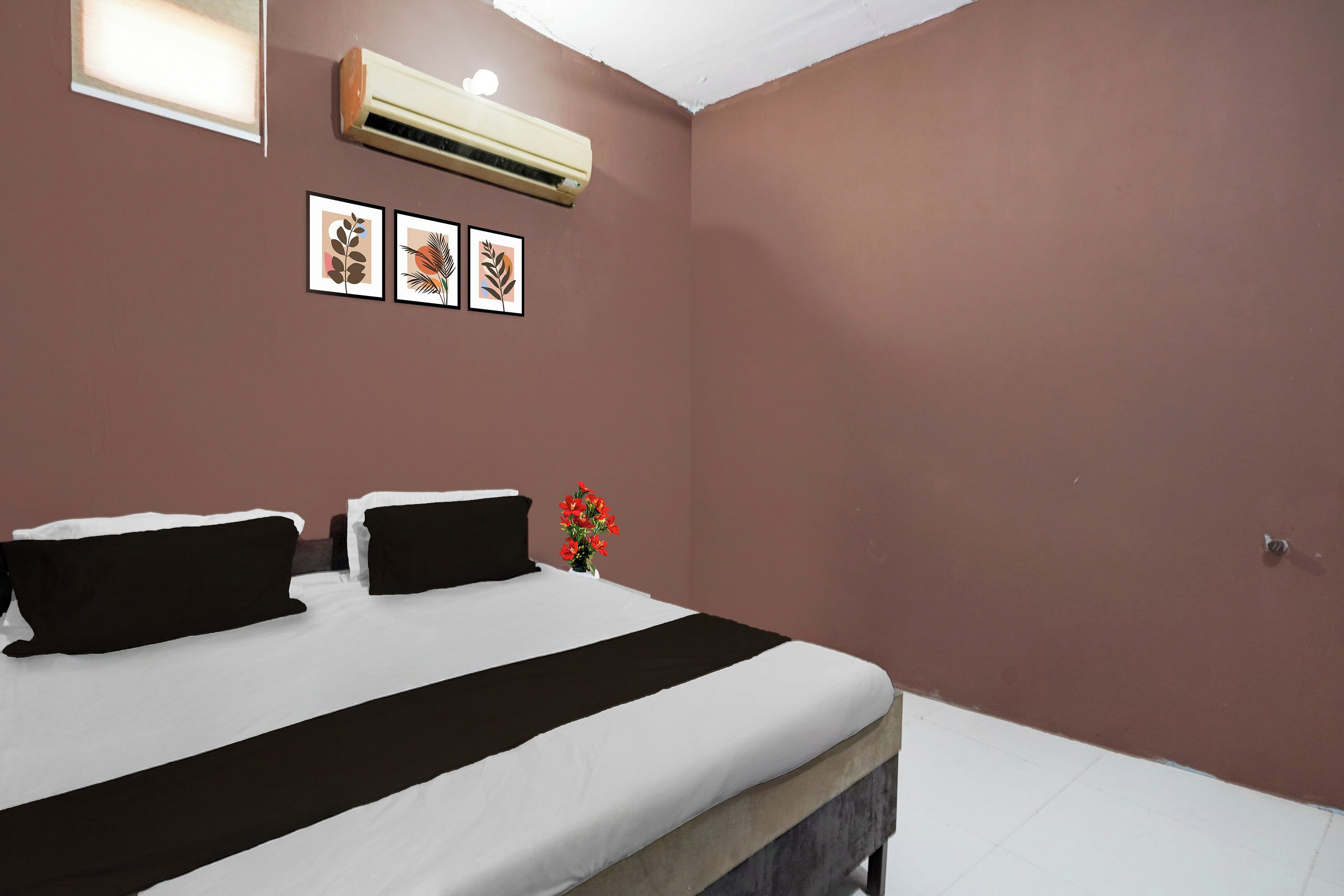Quarto de hotel com uma cama, ar condicionado fixado na parede e três impressões botânicas emolduradas.