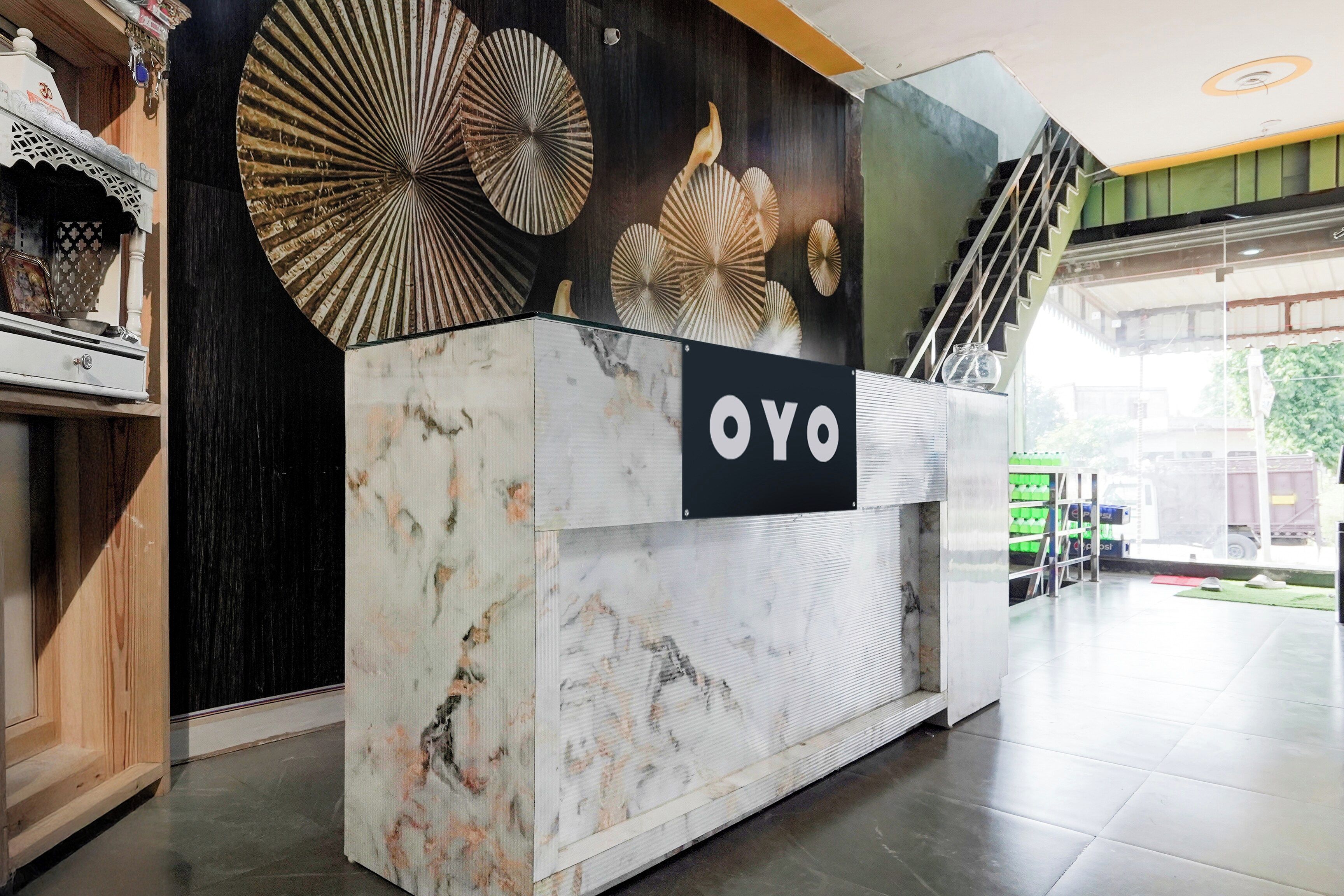 Een receptiebalie met een bordje met de tekst 'OYO' in een moderne lobby met een trap en uitzicht op buiten.