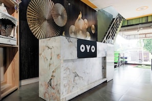 Una taquilla de recepció amb un cartell que diu 'OYO' a un vestíbul modern amb una escala i una vista cap a l'exterior.