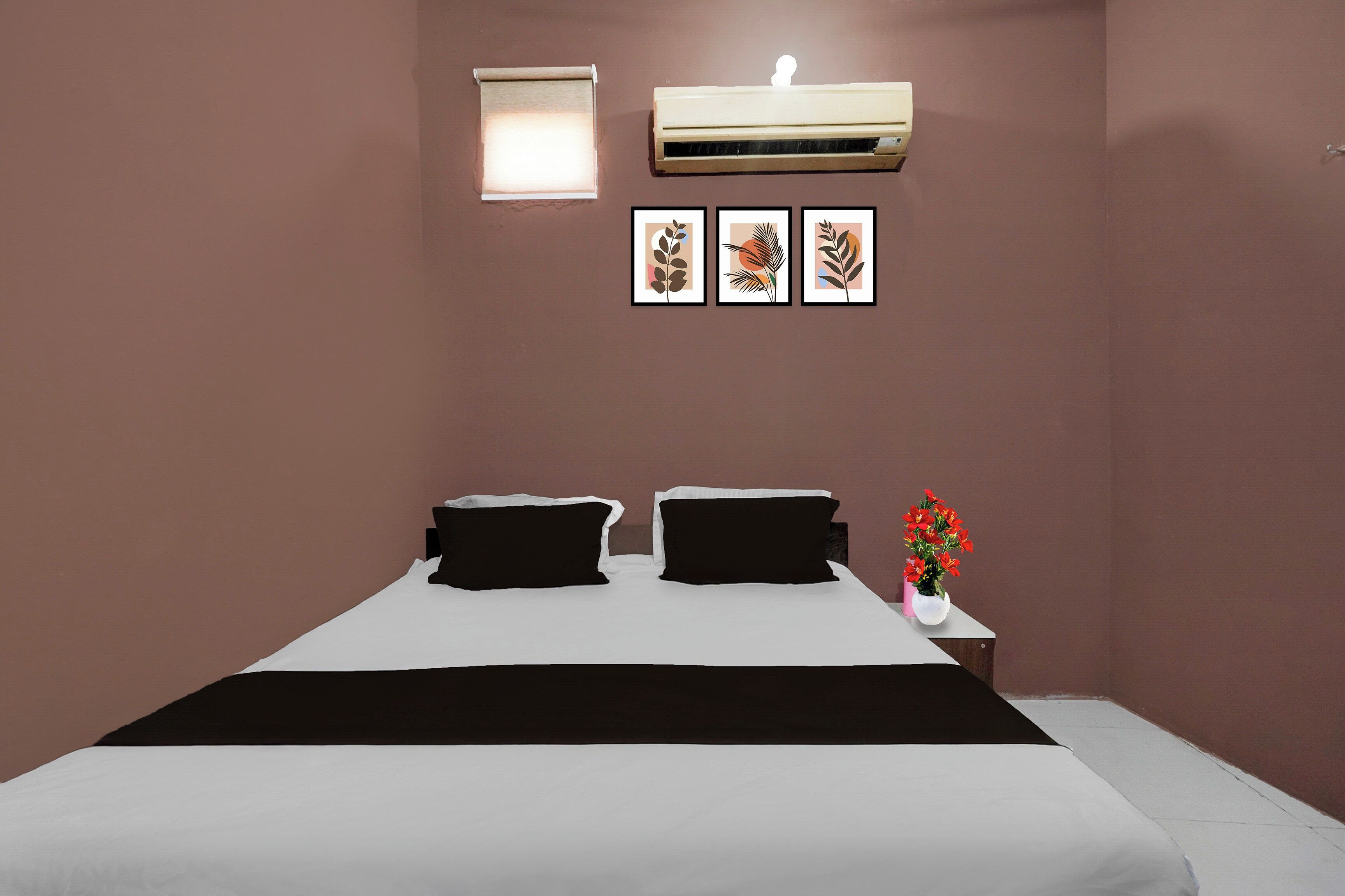 Un dormitorio con cama, dos almohadas, una mesita de noche con un florero y tres cuadros en la pared.