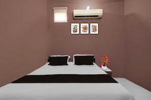A bedroom with a bed, two pillows, a nightstand with a vase of flowers, and three framed pictures on the wall.