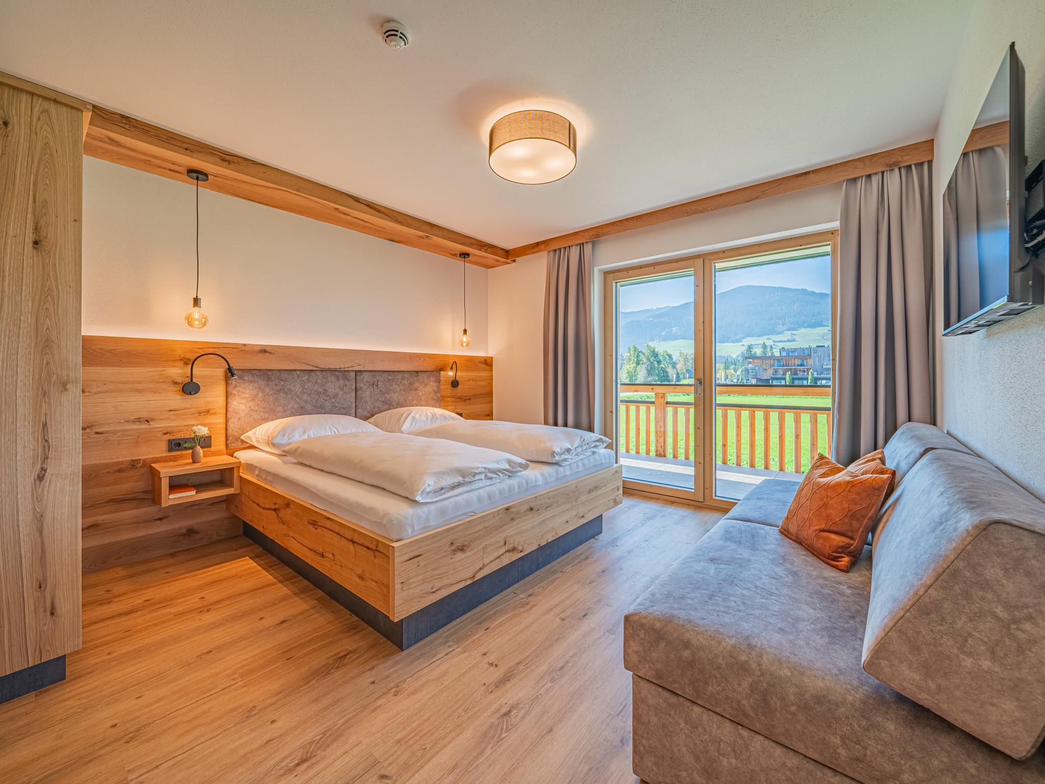 Une chambre à coucher avec un lit en bois, une table de chevet, un canapé et une grande fenêtre donnant sur l’extérieur.
