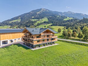 Un edificio de madera de varios pisos con balcones, situado en un paisaje verde con montañas al fondo.