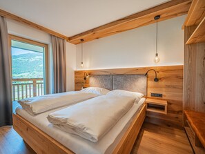 Cama doble con cabecera de madera, dos mesitas de noche y vistas a un balcón.